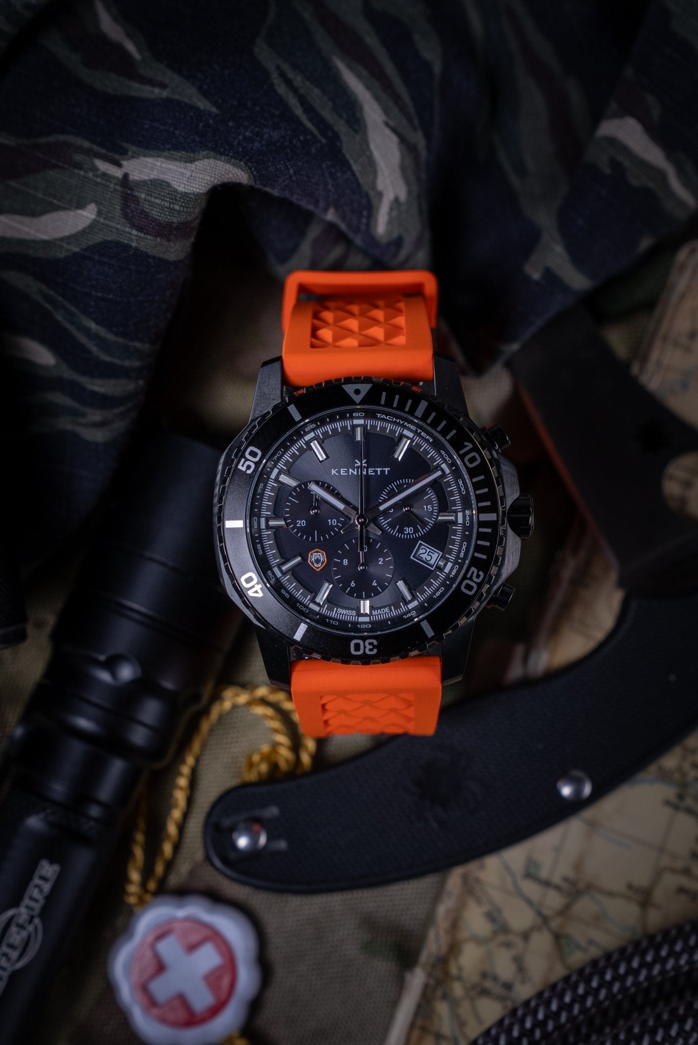 Kennett x Ollie Ollerton Solaforce watch styled with a knife and paracord bracelet on camouflage fabric, reflecting its survival and tactical gear theme