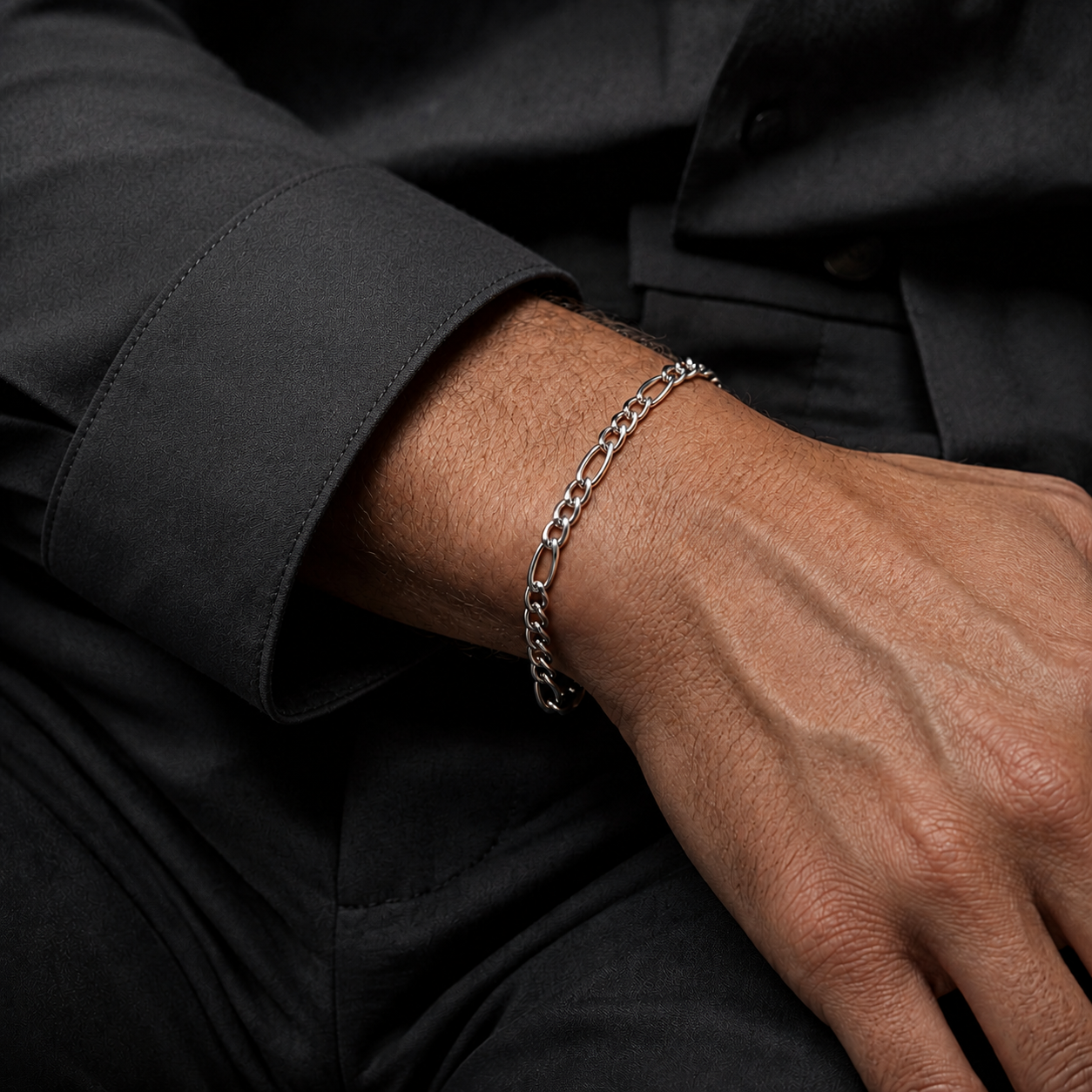 A close-up of a person's wrist wearing a silver chain link bracelet, shown against a dark charcoal gray shirt.