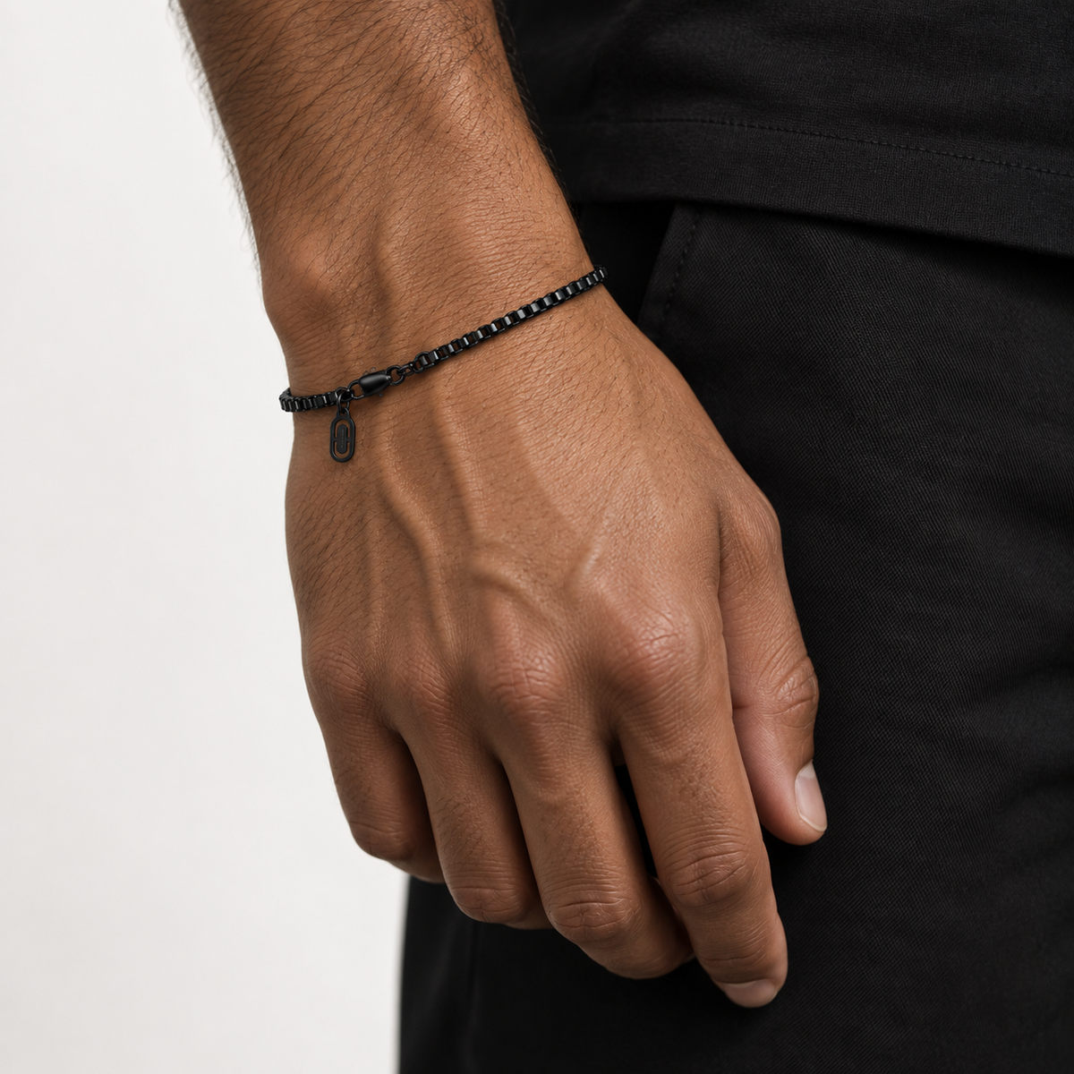 A close-up of a man's hand wearing a black beaded bracelet with a small hanging tag, paired with a black shirt against a light gray background.