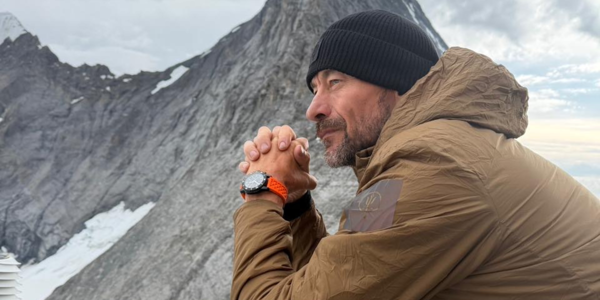 Ollie Ollerton wearing the Kennett x Ollie Ollerton Solaforce limited edition Swiss solar chronograph on a mountain summit, hands clasped, overlooking a jagged peak